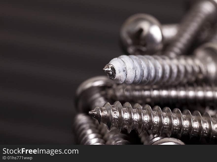 Recycled screws with one showing signs of previous use. Shot with copy space on black to the left of the frame. Drywall dust caked to the threads of a panhead screw in a pile for use again. Recycled screws with one showing signs of previous use. Shot with copy space on black to the left of the frame. Drywall dust caked to the threads of a panhead screw in a pile for use again.