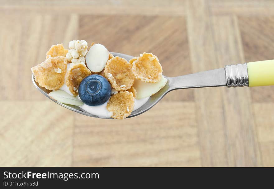 Spoonful of cereal with corn flakes, milk, and a blueberry