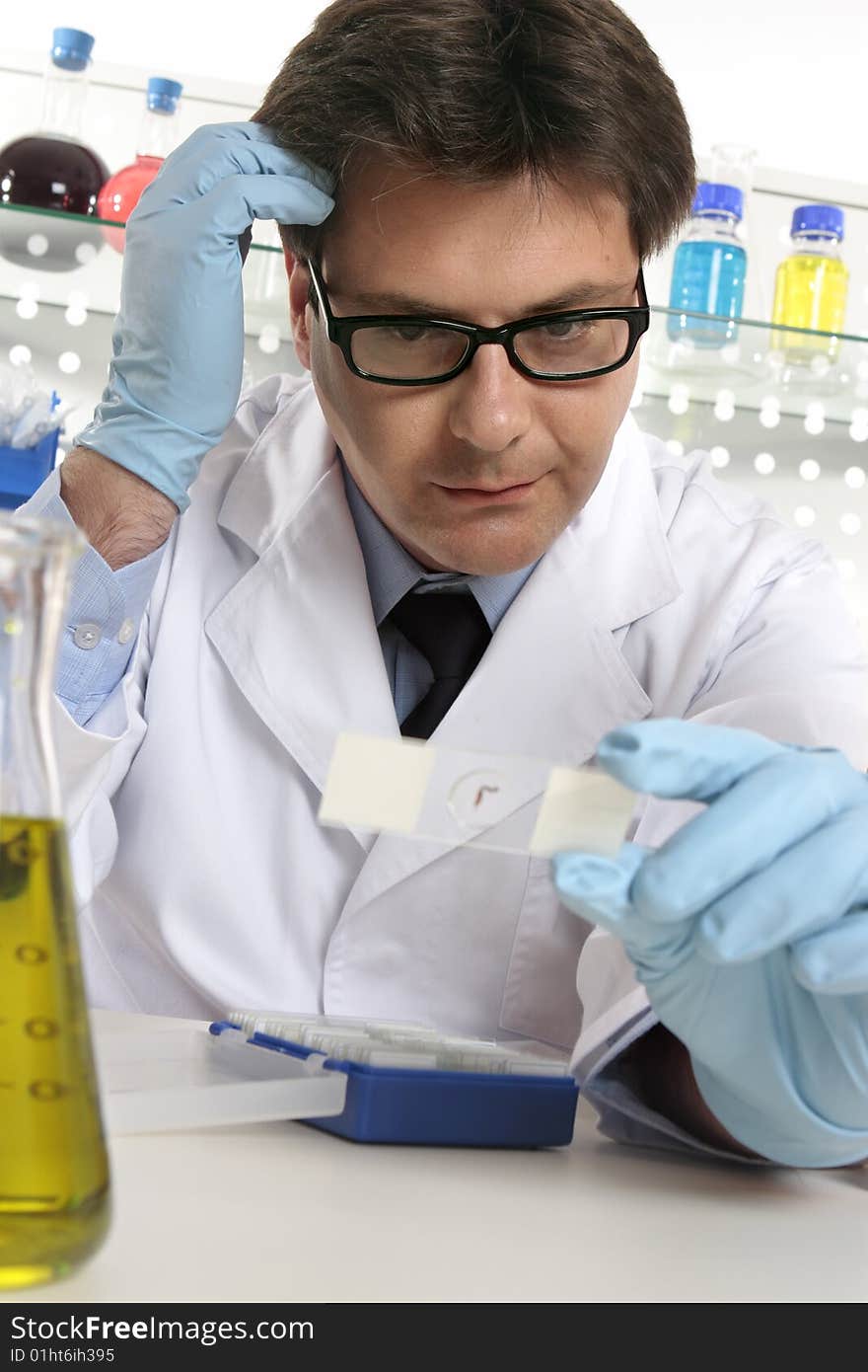 A scientist scratches his head whilst examining a microscope slide. A scientist scratches his head whilst examining a microscope slide.