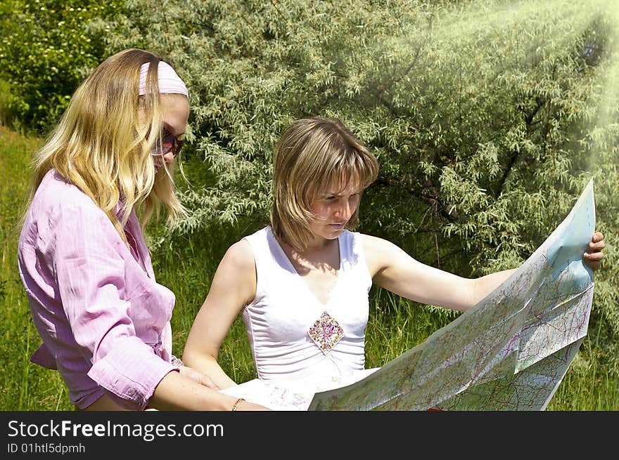 Two beautiful girls look at the map on nature