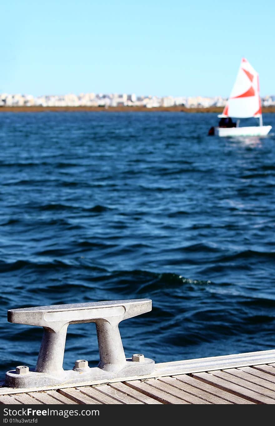 Detail of an modern anchoring spot, on the background unfocused there's a small sailing boat and the city.