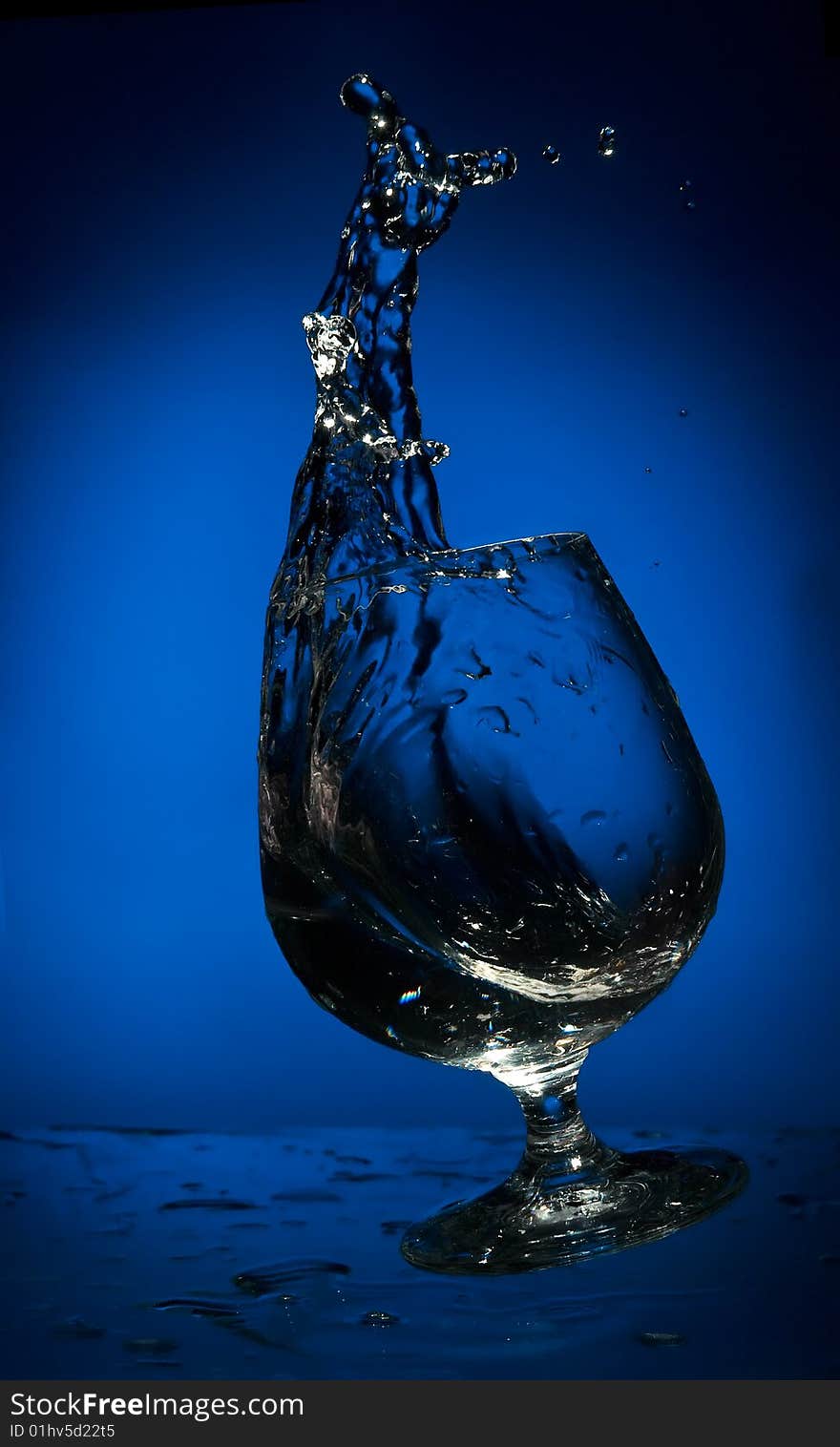 Frozen by flash big splash of fluid in a falling glass on the blue background