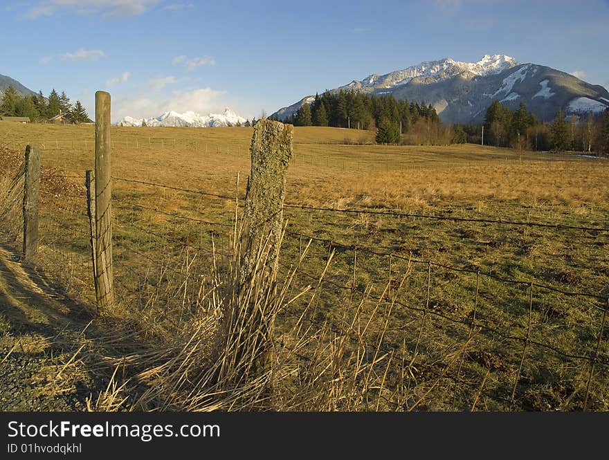 A fenced field gives way to distant snow-capped mountains. A fenced field gives way to distant snow-capped mountains.