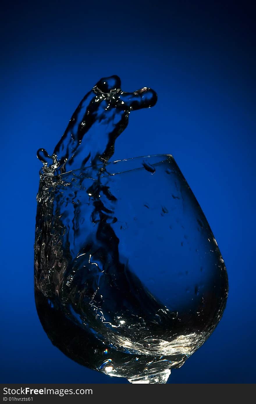 Frozen by flash big splash of fluid in a glass  on the blue background. Frozen by flash big splash of fluid in a glass  on the blue background