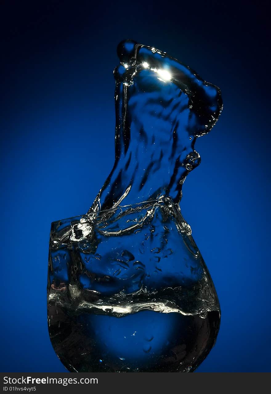 Frozen by flash big splash of fluid in a glass  on the blue background. Frozen by flash big splash of fluid in a glass  on the blue background