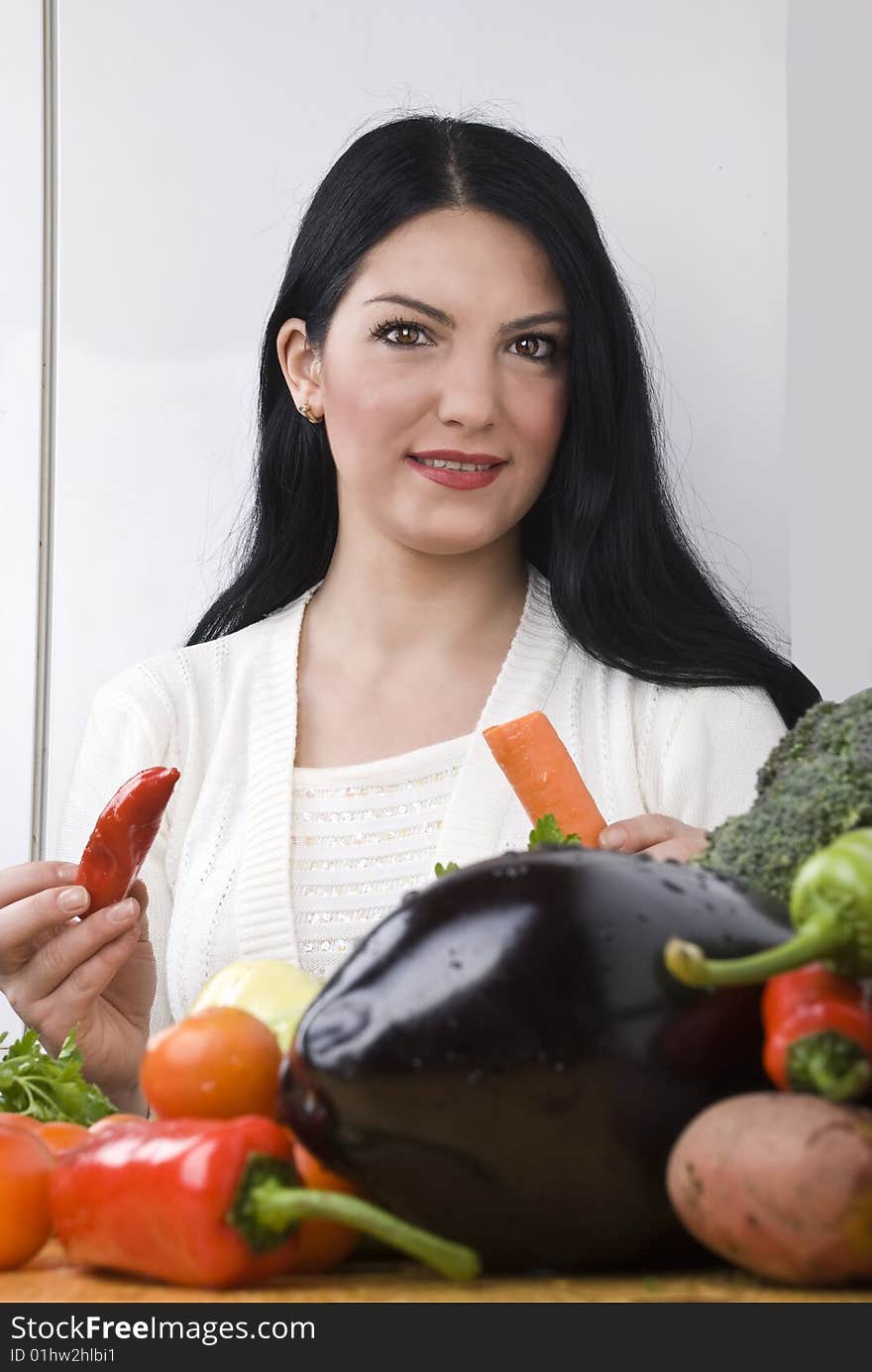 Young brunette woman in kitchen with fresh vegetables holding a red pepper and a carrot.Check out also Healthy food. Young brunette woman in kitchen with fresh vegetables holding a red pepper and a carrot.Check out also Healthy food