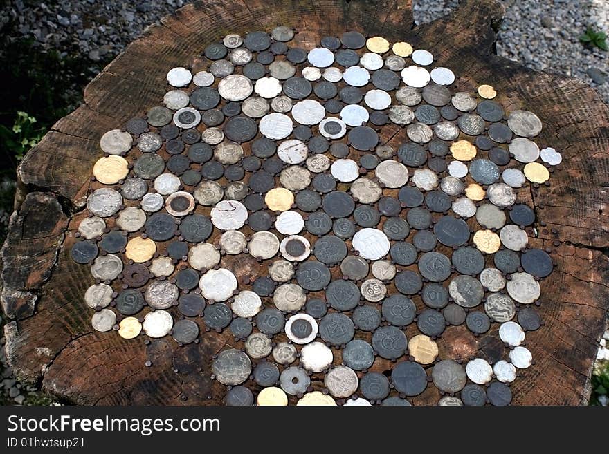 All kind of coins, old and new, fixed in a stump of a tree with rusty nails, making a table. All kind of coins, old and new, fixed in a stump of a tree with rusty nails, making a table.