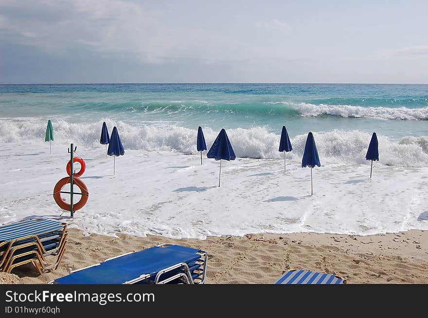 Storm approaching: umbrellas on the beach overtaken by rough sea. Storm approaching: umbrellas on the beach overtaken by rough sea