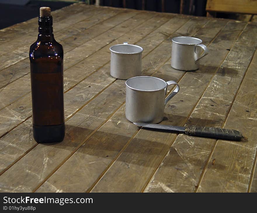 Three mugs, knife and bottle of whisky on a wooden table. Three mugs, knife and bottle of whisky on a wooden table