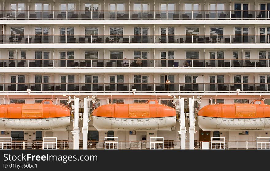 The side of a cruise ship showing balconies and lifeboats