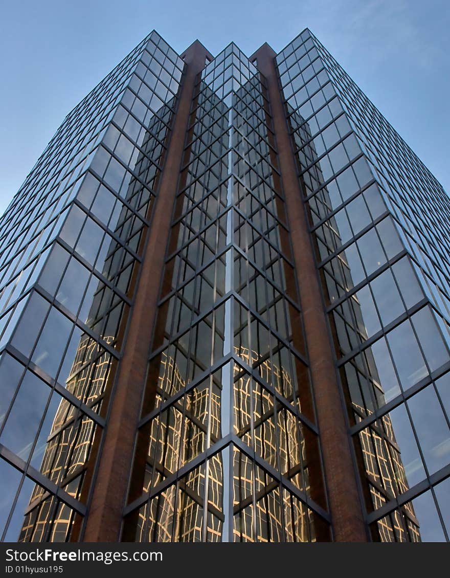 Looking up at a modern skyscraper with a building reflected in it's tinted glass windows.