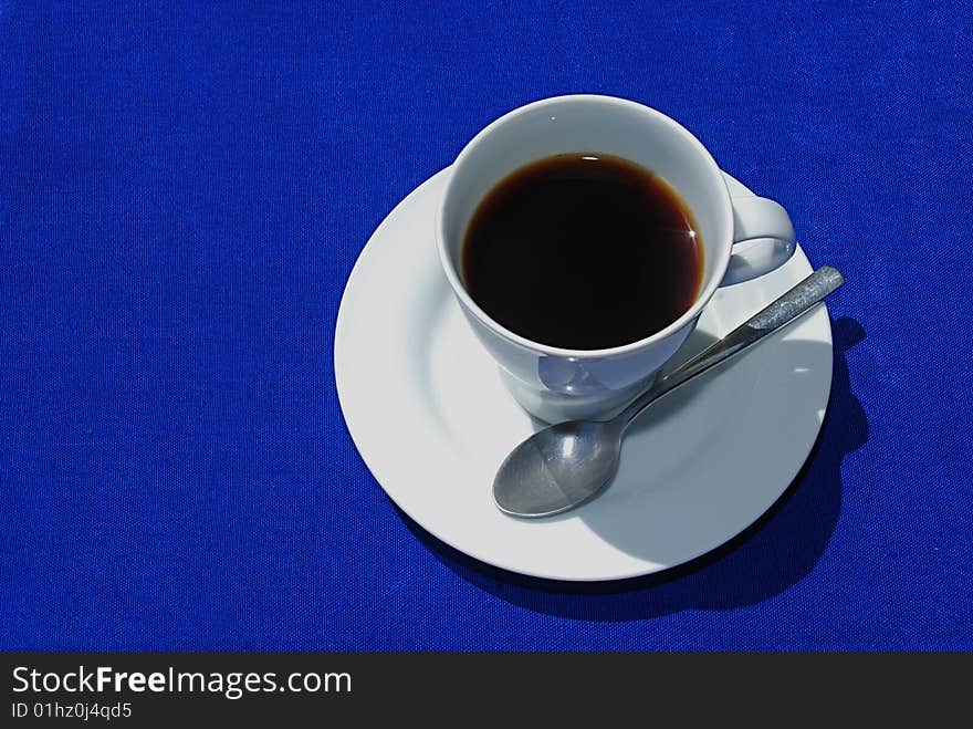 Black coffee in white cup with plate and spoon on blue background