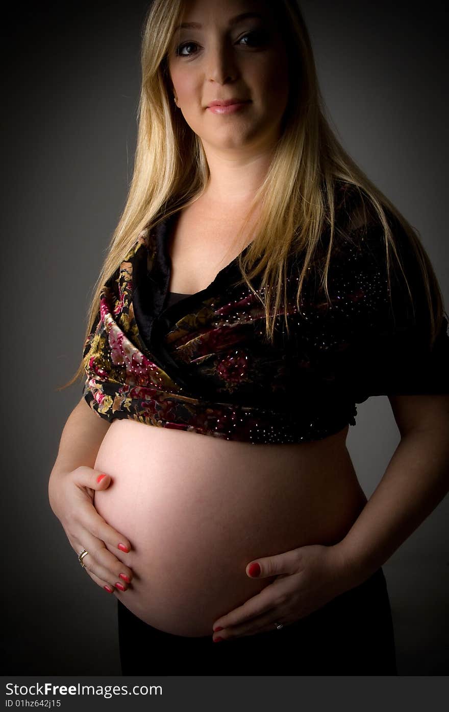 Side view of smiling pregnant female holding her tummy on an isolated background