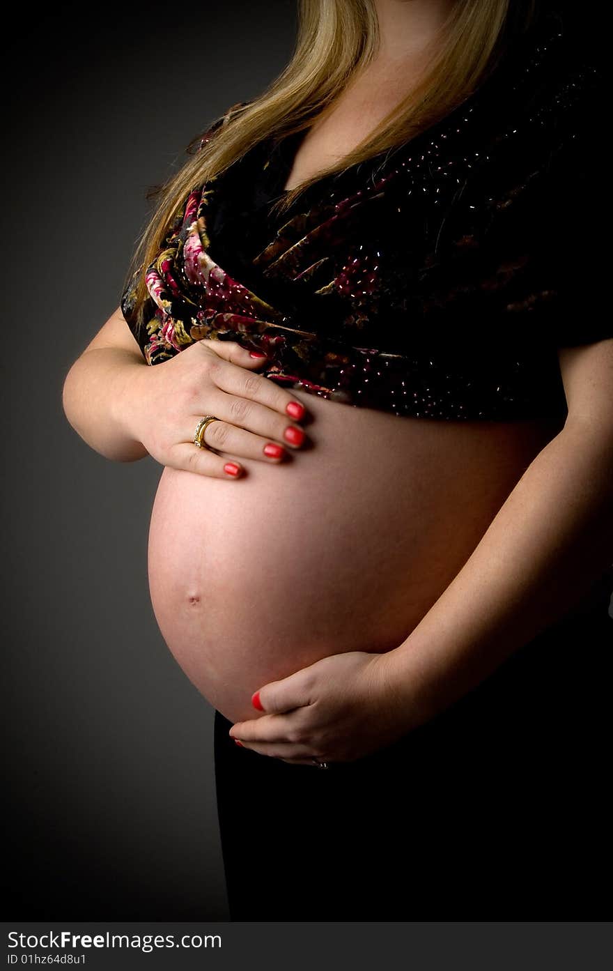 Side view of pregnant female holding her tummy against white background