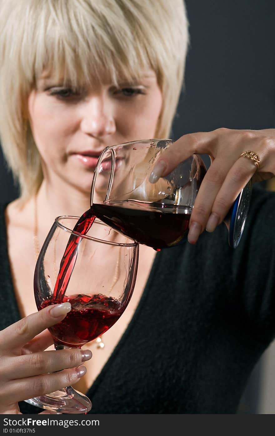 The blonde pours from a glass in a glass red wine. The blonde pours from a glass in a glass red wine.