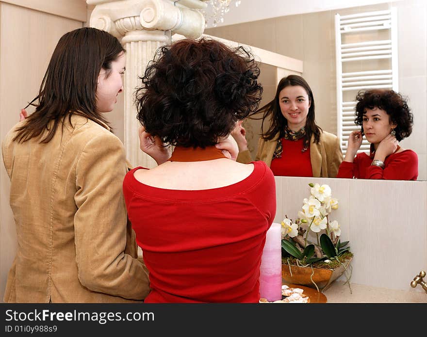 Two young women in front of a mirror arranging themselves. Two young women in front of a mirror arranging themselves