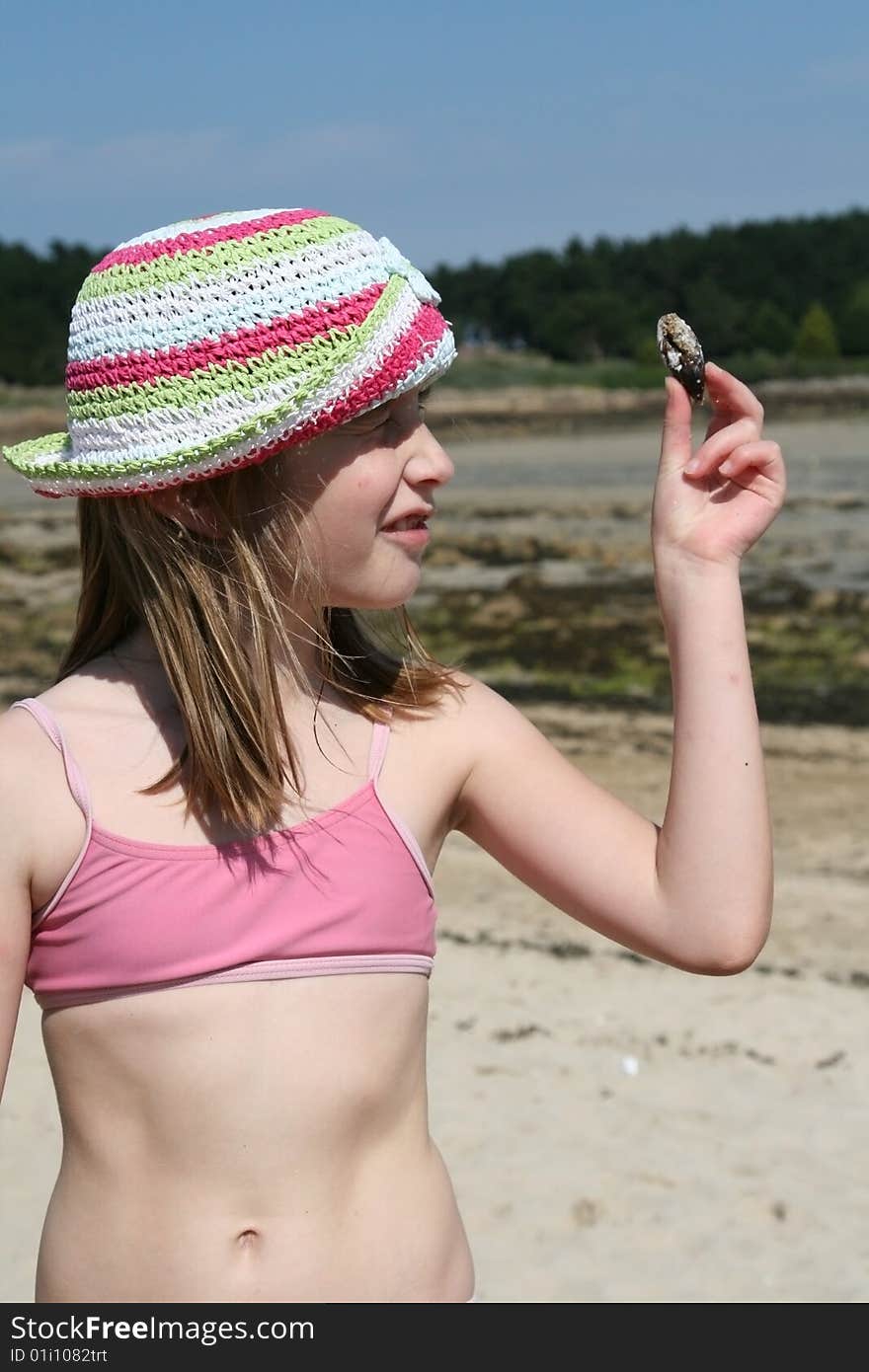 Teenage girl looking at a shell on the beach