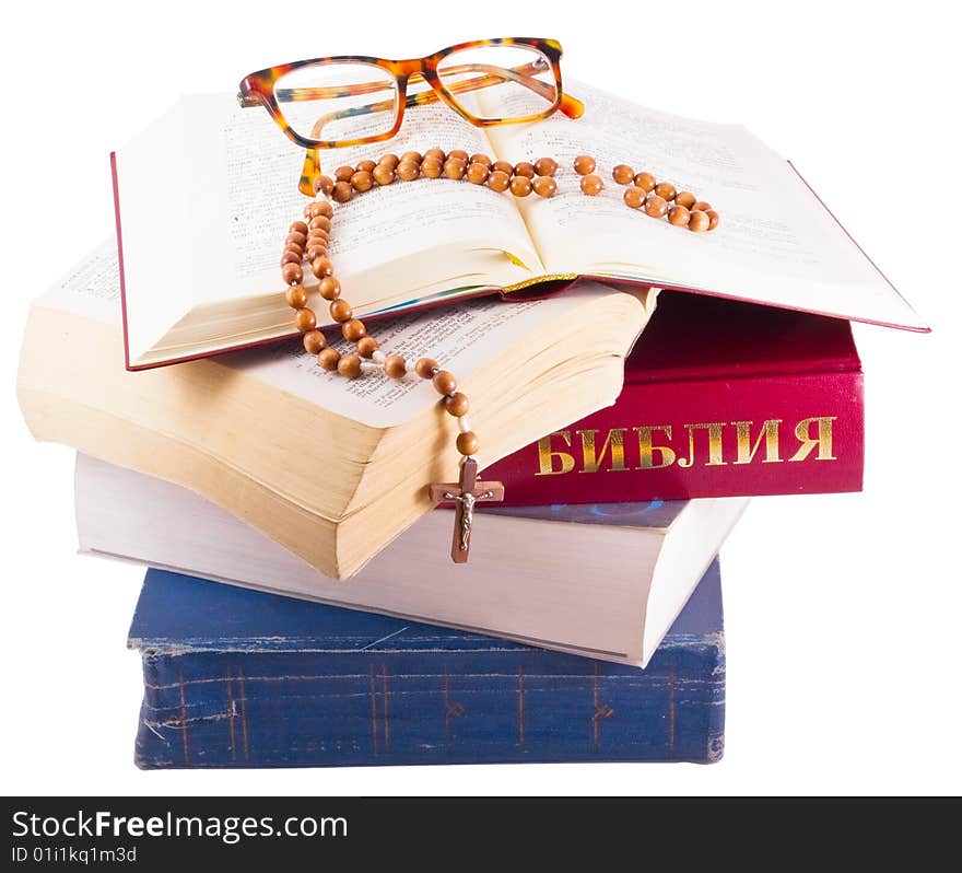 Open Holy Bible lying on stack of old books with glasses, cross and beads isolated. Open Holy Bible lying on stack of old books with glasses, cross and beads isolated