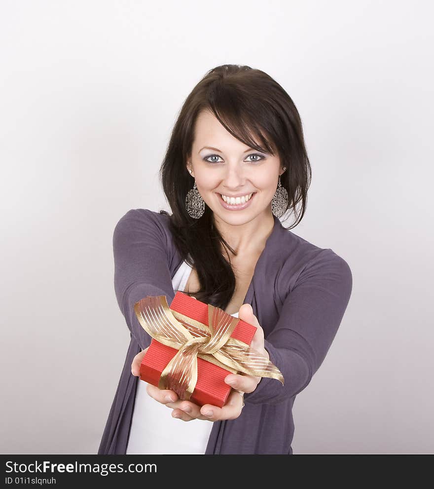 A beautiful brunette holds out a ribbon wrapped gift. It is for you!