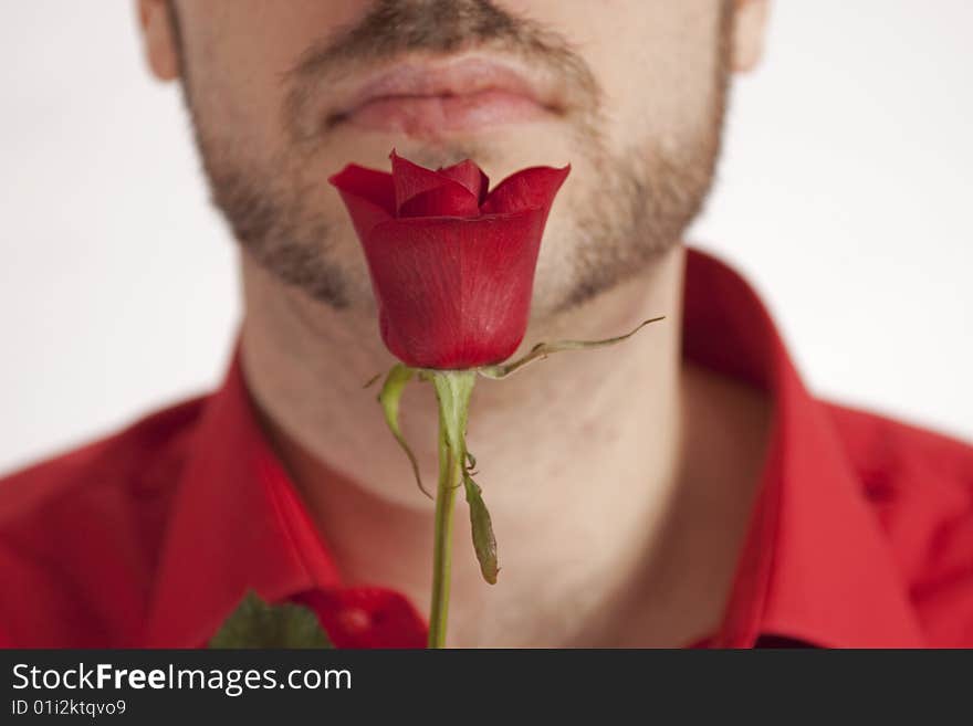 A man, holding a beautiful red rose in front of his face, wearing a red shirt. A man, holding a beautiful red rose in front of his face, wearing a red shirt