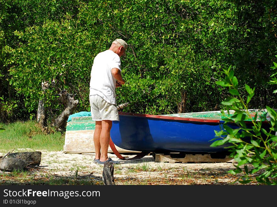 Senior man repairing small blue boat on island beach. Senior man repairing small blue boat on island beach.