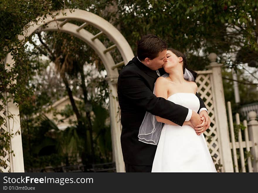 Newlyweds kissing in garden with arbor in background. Newlyweds kissing in garden with arbor in background