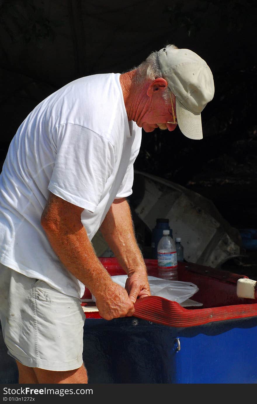 Senior man repairing small blue boat on island beach. Senior man repairing small blue boat on island beach.