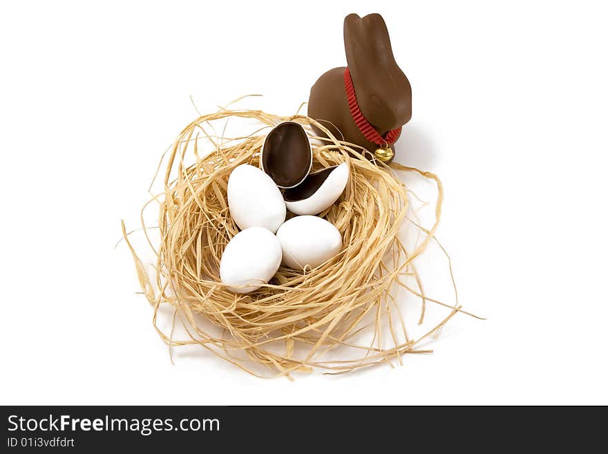 Chocolate Easter bunny looking over straw nest with white coated chocolate eggs, one hatched, on white background. Chocolate Easter bunny looking over straw nest with white coated chocolate eggs, one hatched, on white background.