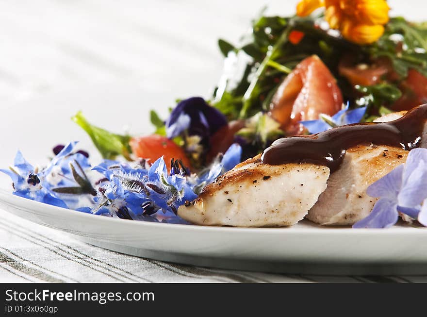 Grilled chicken breast served with salad and garnished with edible flowers