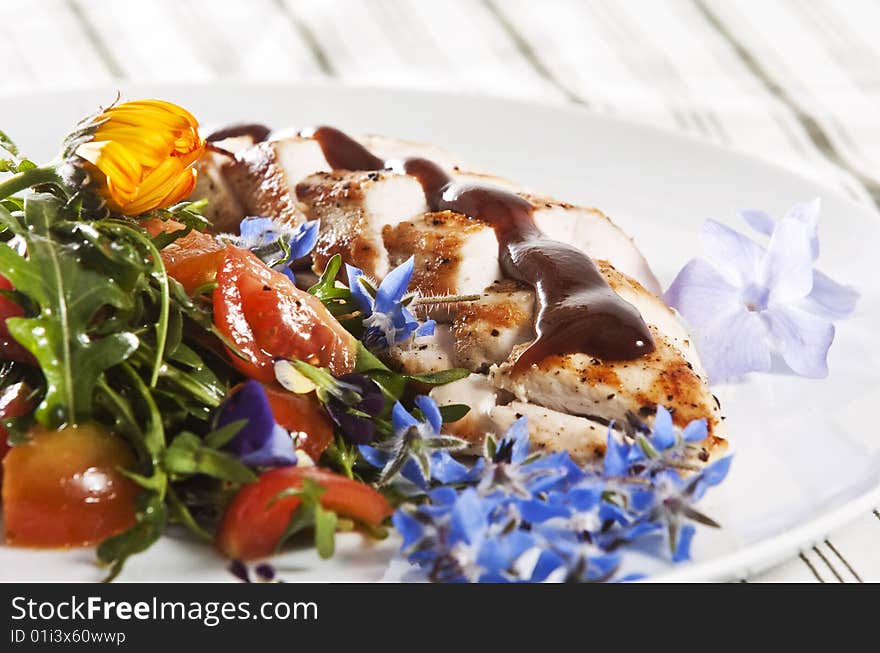 Grilled chicken breast served with salad and garnished with edible flowers