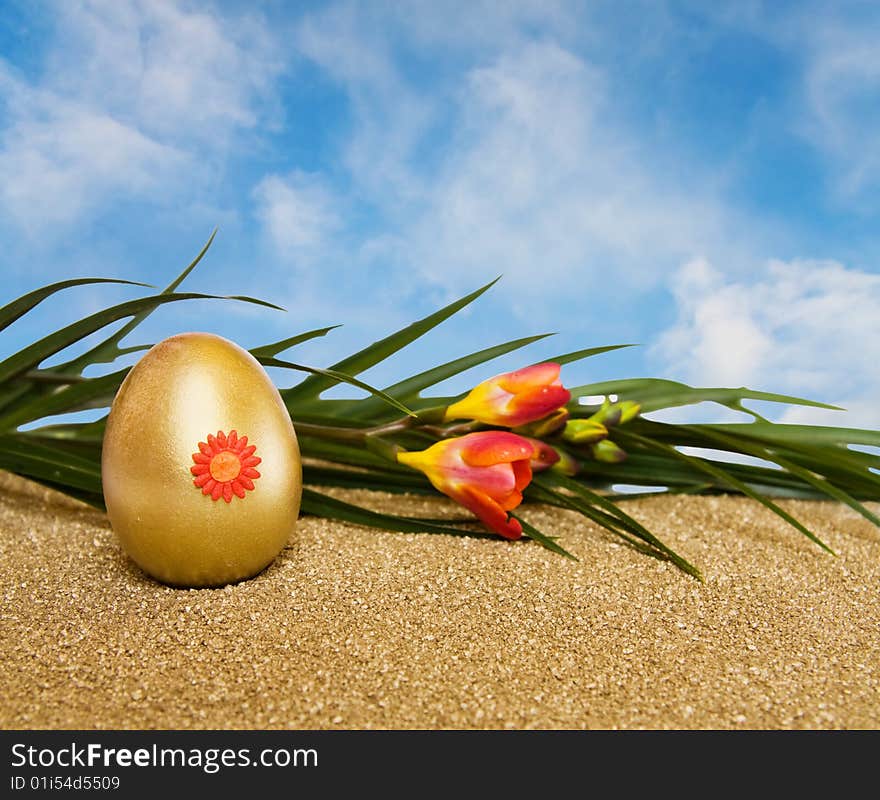 Celebrating Easter with golden decorated egg and spring freesia flowers over blue sky with room for your text. Celebrating Easter with golden decorated egg and spring freesia flowers over blue sky with room for your text.