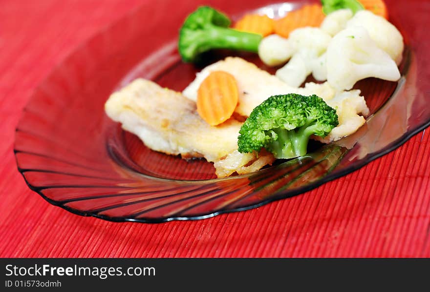 Plate with fish and vegetables on red table. Plate with fish and vegetables on red table