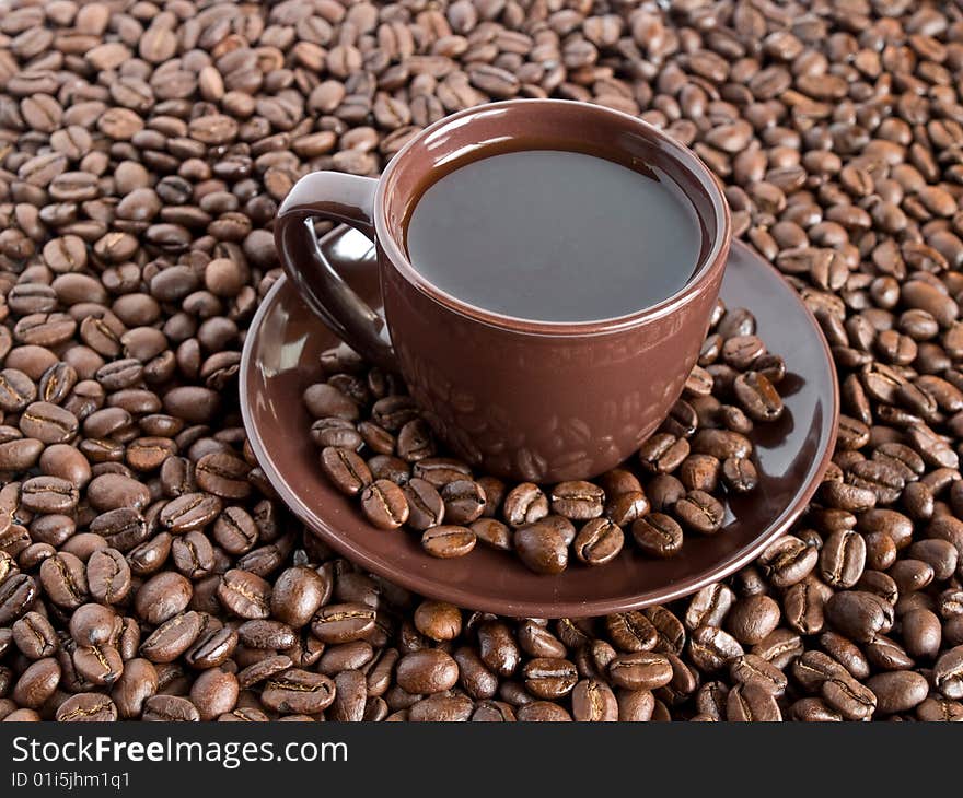 A close-up composition of a cup of coffee with saucer and being surrounded with coffee beans. A close-up composition of a cup of coffee with saucer and being surrounded with coffee beans