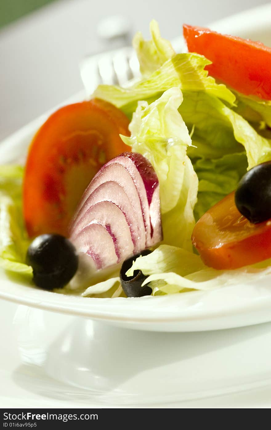 Fresh salad with onion tomato and olives in a white plate