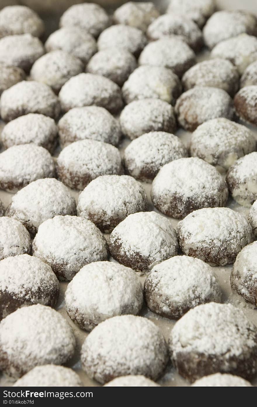 Lines of dark chocolate cookies, fresh out of the oven at a bakery. Dusted with icing suger. Lines of dark chocolate cookies, fresh out of the oven at a bakery. Dusted with icing suger.