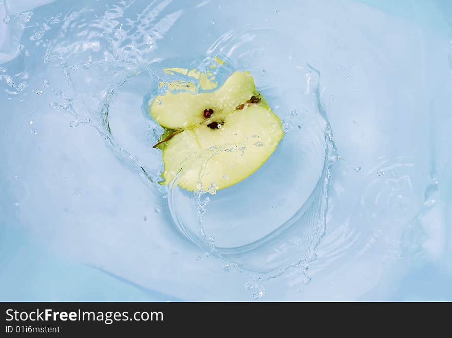 Green apple falling into blue water