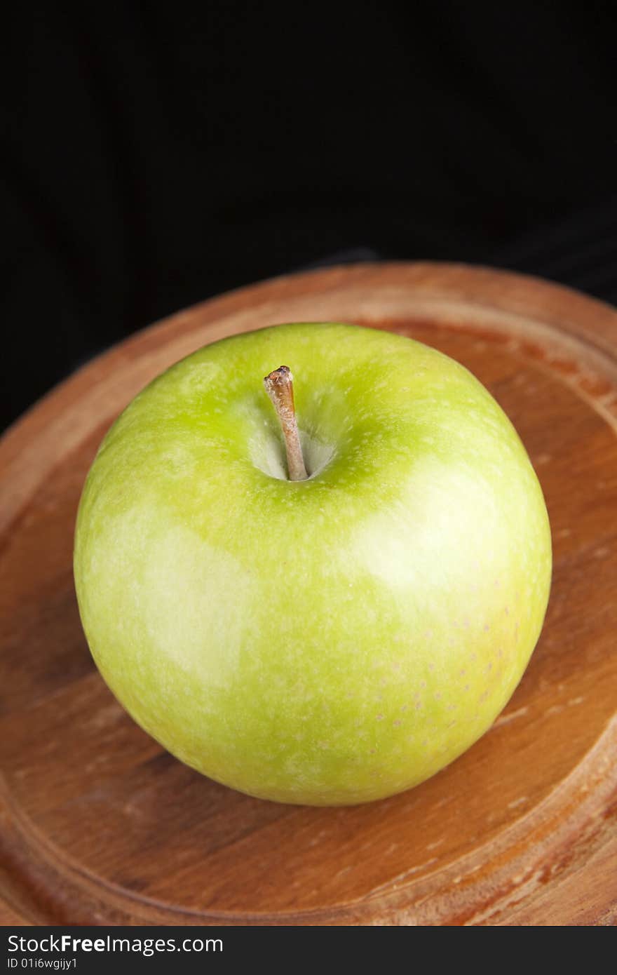 Granny smith green apple on a wooden platter against a black background. Granny smith green apple on a wooden platter against a black background