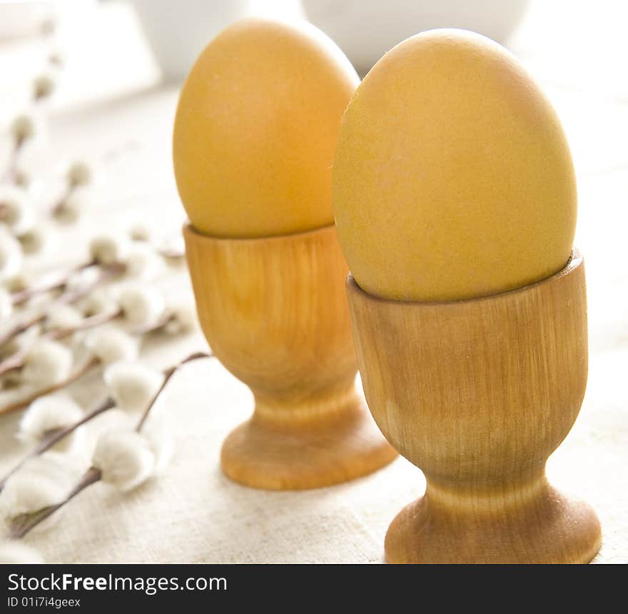 Yellow easter eggs in wooden cups and some catkins on table cloth