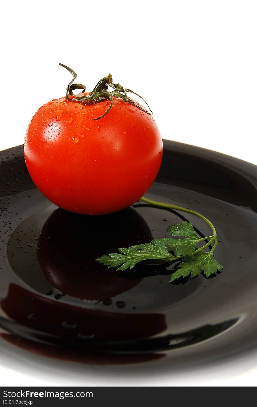 Wet red tomato with parsley on the black table. White bacjground. Drops on the tomato. Wet red tomato with parsley on the black table. White bacjground. Drops on the tomato.