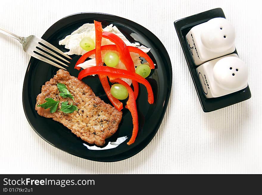 Tasty pork chop with fresh salad (red pepper, green grape and chinese cabbage) on the ribbed linen napkin. View from above. Tasty pork chop with fresh salad (red pepper, green grape and chinese cabbage) on the ribbed linen napkin. View from above.