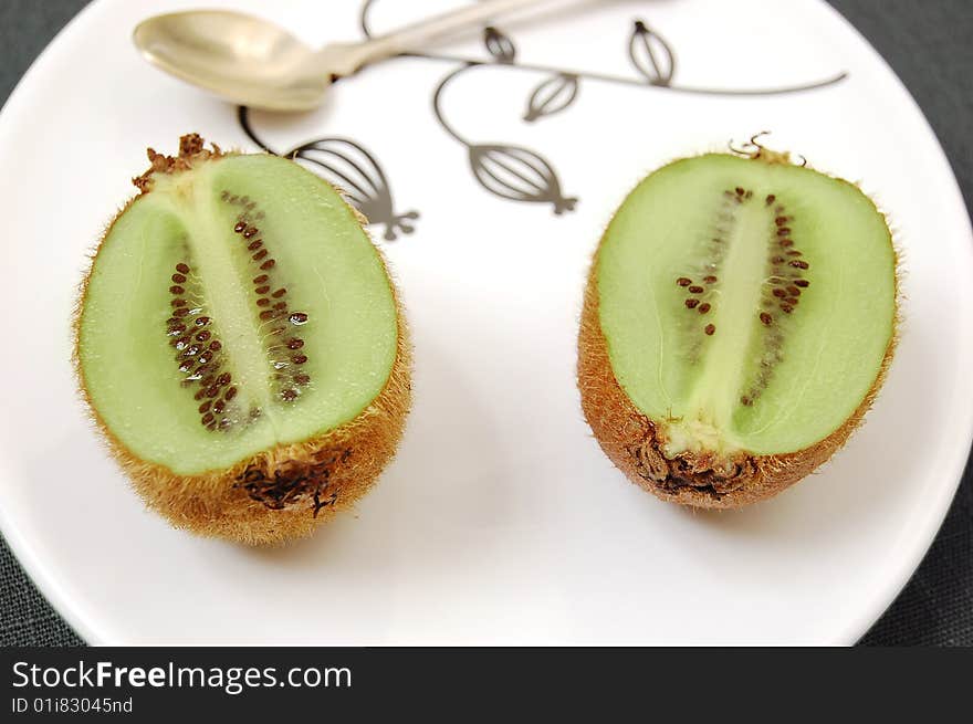 Two half kiwifruit on the white dessert-plate view from above.