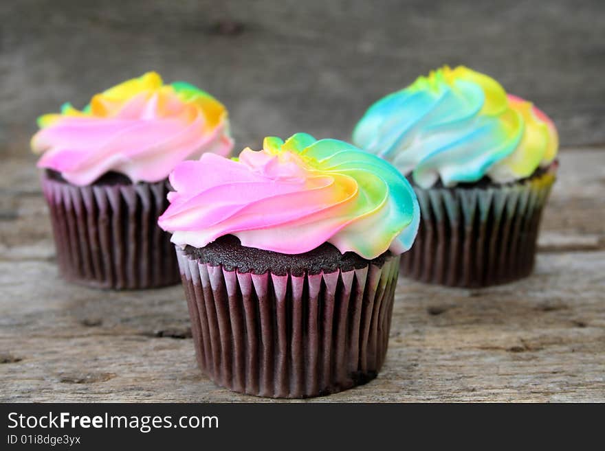 Chocolate cupcakes with multi colored icing shot on a rustic background.