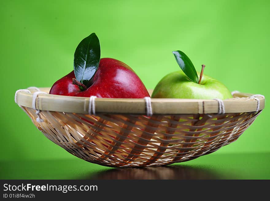 Green and red apples in basket, green background