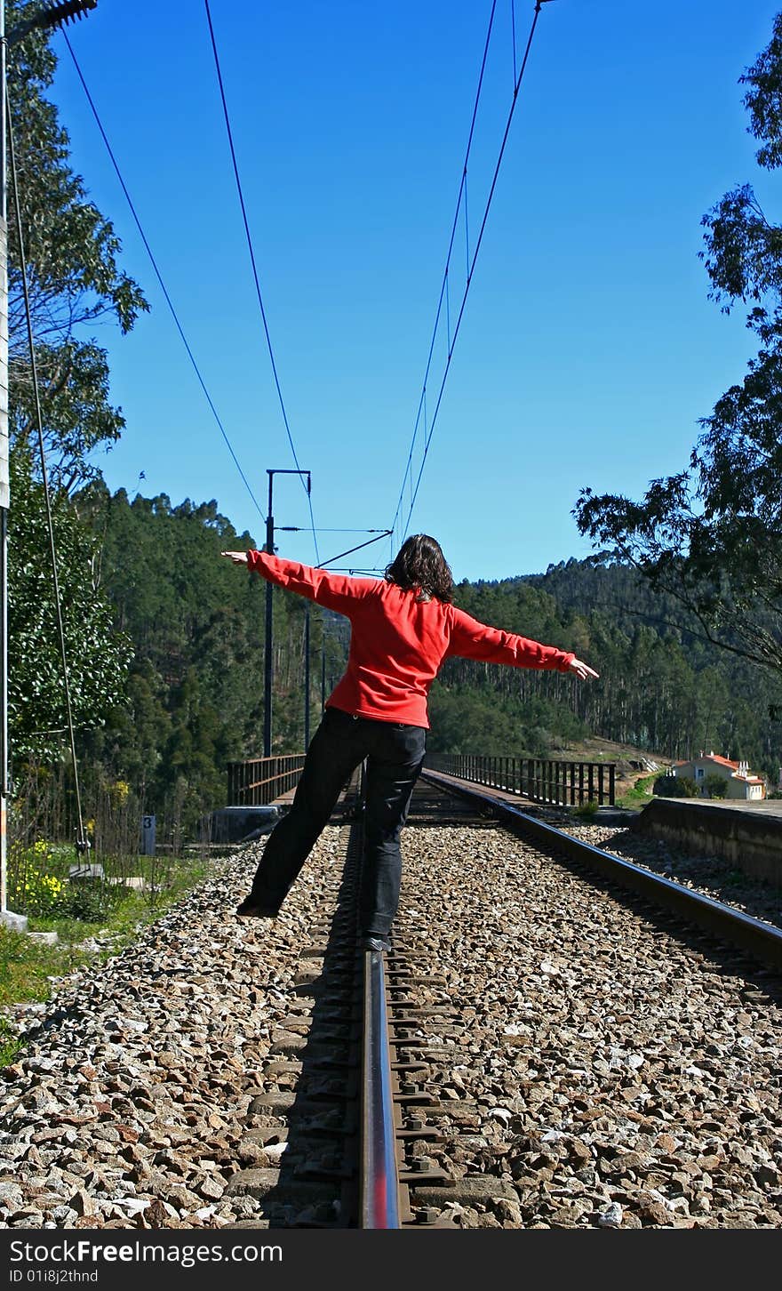 Woman in red, with arms open, walking in the railway