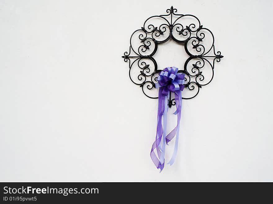 Iron ornament with a purple ribbon hanging on a white wall. Iron ornament with a purple ribbon hanging on a white wall