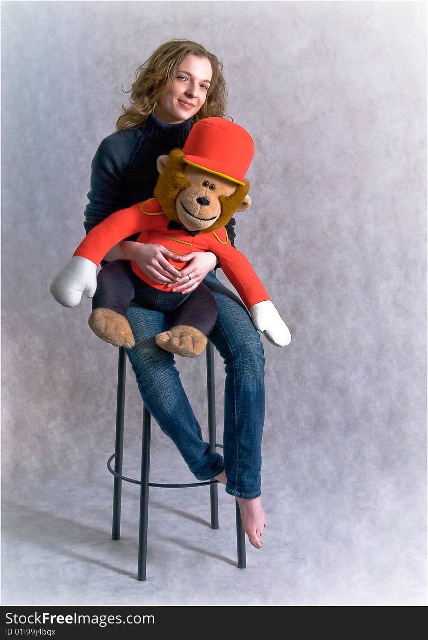 Beautiful smiling girl is sitting on a chair embracing toy red big monkey. Beautiful smiling girl is sitting on a chair embracing toy red big monkey.