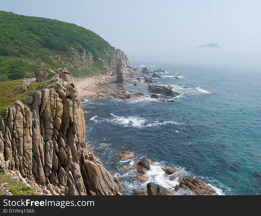 A rocky cliff on Japanese sea. On background are surf and rocks in fog. A rocky cliff on Japanese sea. On background are surf and rocks in fog.