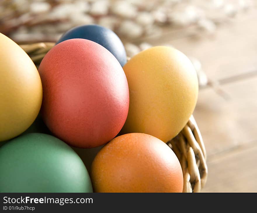 Colorful easter eggs in a basket on wooden boards. Some catkins in background.