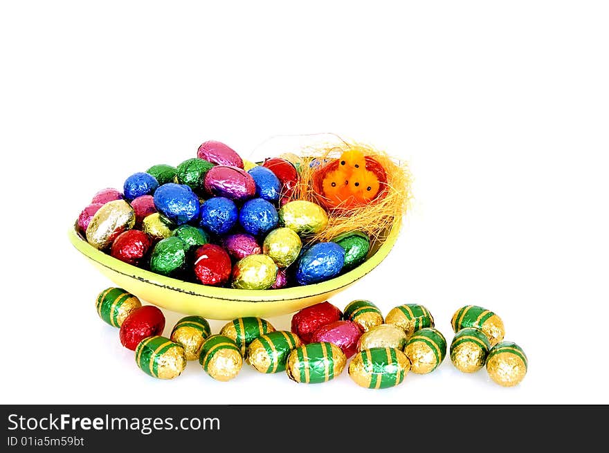 Bowl filled with colorfull wrapped chocolate easter eggs on white background, reflective surface. Bowl filled with colorfull wrapped chocolate easter eggs on white background, reflective surface