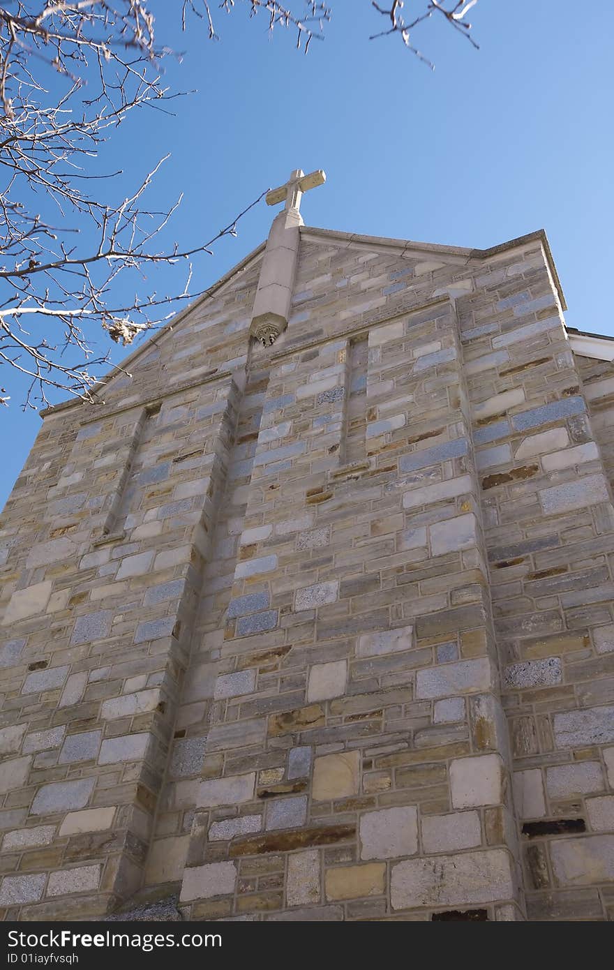 From an extreme low angle a great perspective of the front of a church and the cross which is on top, all framed by branches of a tree and a beautiful blue sky. From an extreme low angle a great perspective of the front of a church and the cross which is on top, all framed by branches of a tree and a beautiful blue sky